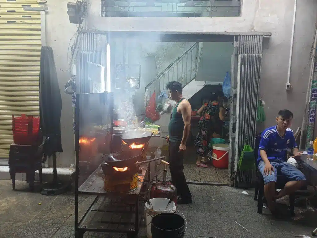 En mann steker mat i en wok på fortauet i Saigon
